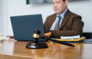 A man on a laptop preparing court paperwork with a gavel on the desk