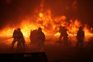 Firefighters putting out a fire in water with fire in the background