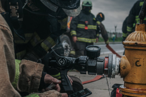 Firefighter connecting a fire hose to a fire hydrant with teammates in the background