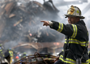 FDNY firefighter on the job at a burnsite pointing at something.